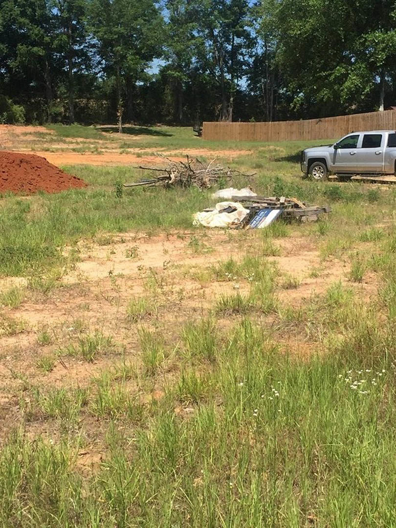 Silver pickup truck parked on grassy field near a pile of dirt, with wooden fence and trees in the background