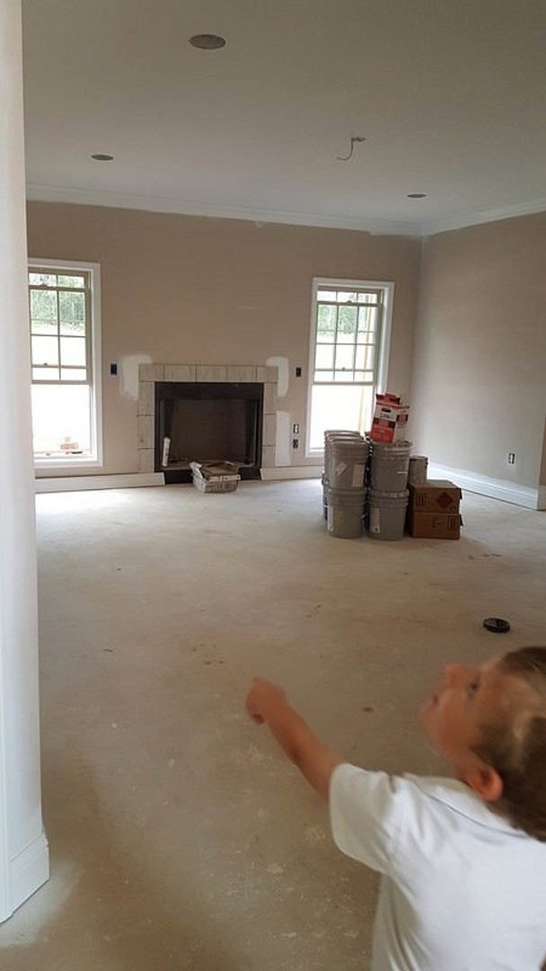 Child playing in a bright room with light wood flooring, several paint buckets, a black fireplace with a white accent, and a white door with glass panes.