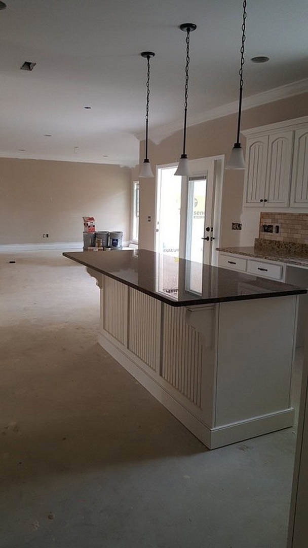 Modern kitchen featuring a black countertop island, white cabinetry, stainless steel sink, pendant chandelier, and large window with natural light.