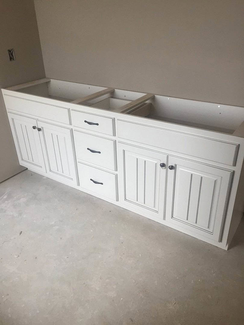 White kitchen cabinetry with black handles, white countertop, and drawers in a bright indoor space with light flooring