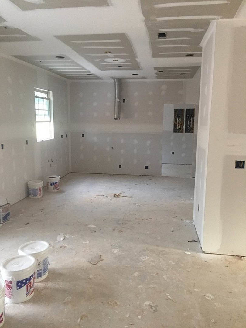 Unfinished room with white walls, scattered paint cans and buckets, sunlight streaming through window, white containers with lids, black object in corner