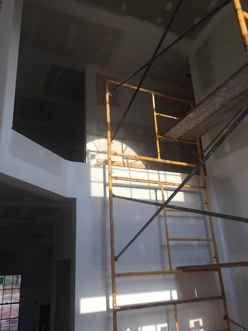 Scaffolding set up in a room with exposed wooden beam, wooden floor, close-up window, metal beam on staircase, and yellow pipe running along a white wall