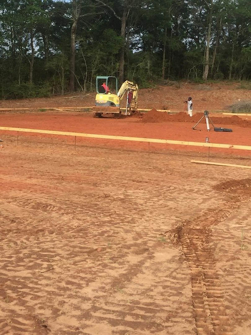 Bulldozer grading soil on residential construction site bordered by trees, visible tire tracks in dirt