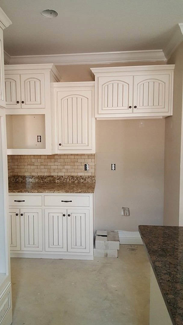 White kitchen cabinets with polished marble countertops, stainless steel sink, tile backsplash, and light wood flooring