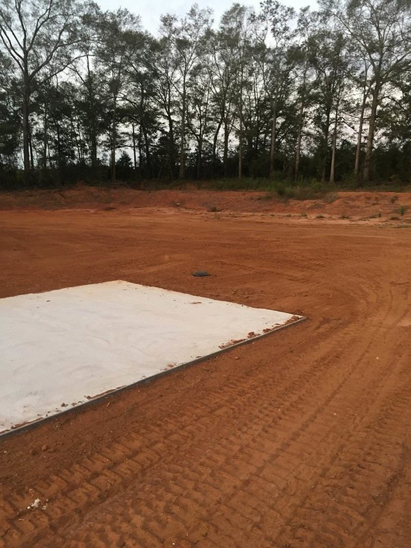Dirt field with a white square plate in the foreground, leafless trees and blue sky in the background