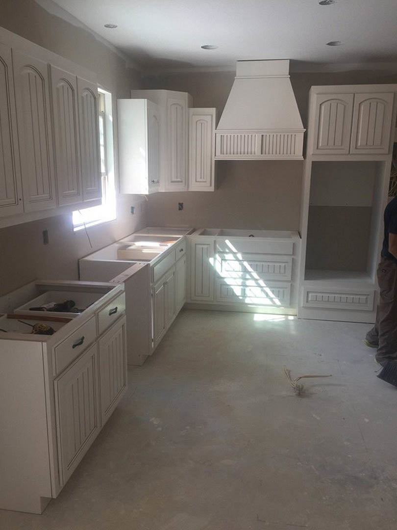 White kitchen with shaker cabinets, quartz countertops, stainless steel appliances, vent hood, and wood flooring