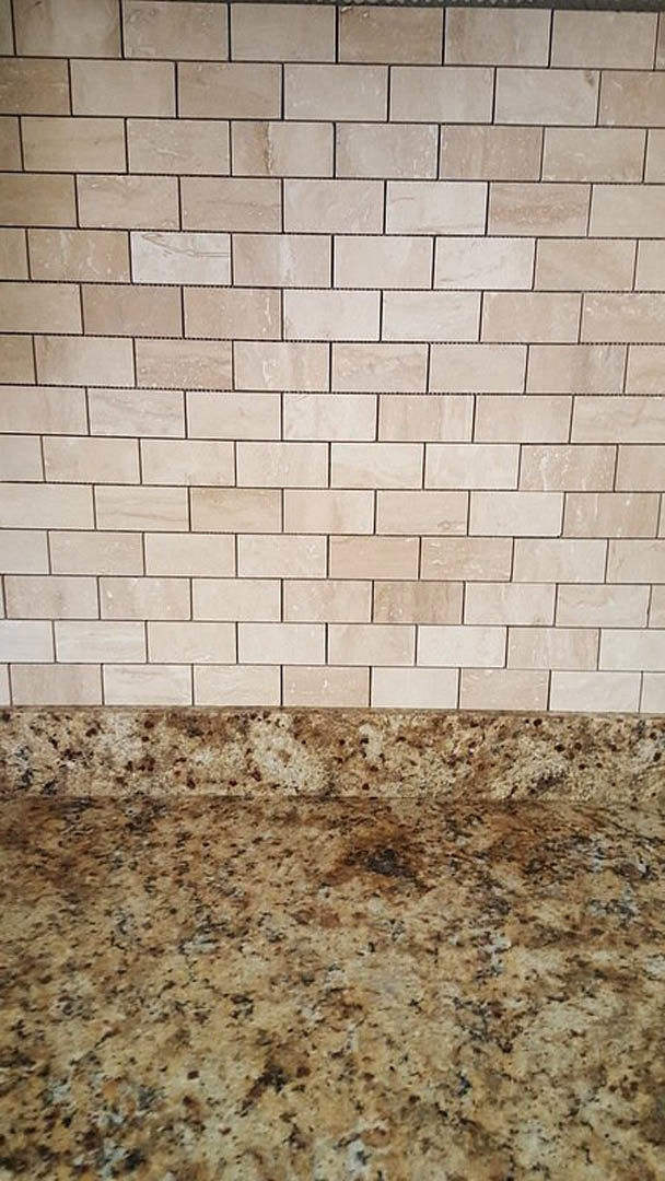 Marble countertop set against a tan brick wall with tile backsplash and white surface featuring black veining