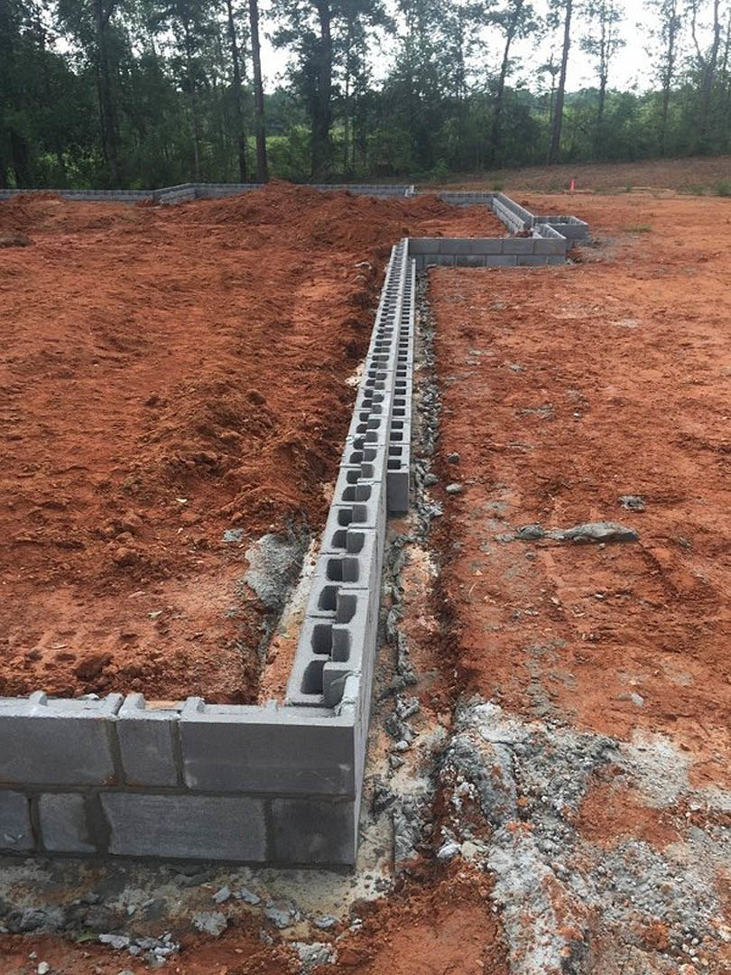Concrete block wall set in red dirt field with sparse grass and trees in background under open sky