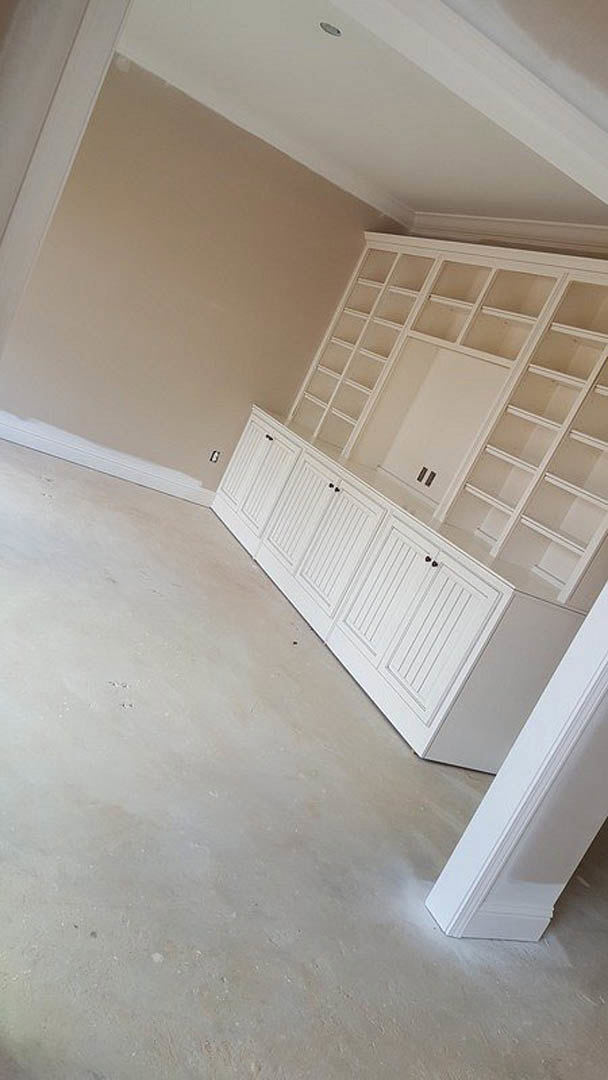 White built-in shelves with glass doors and two open shelves, white cabinets below, white baseboard and plaster walls in a bright room.