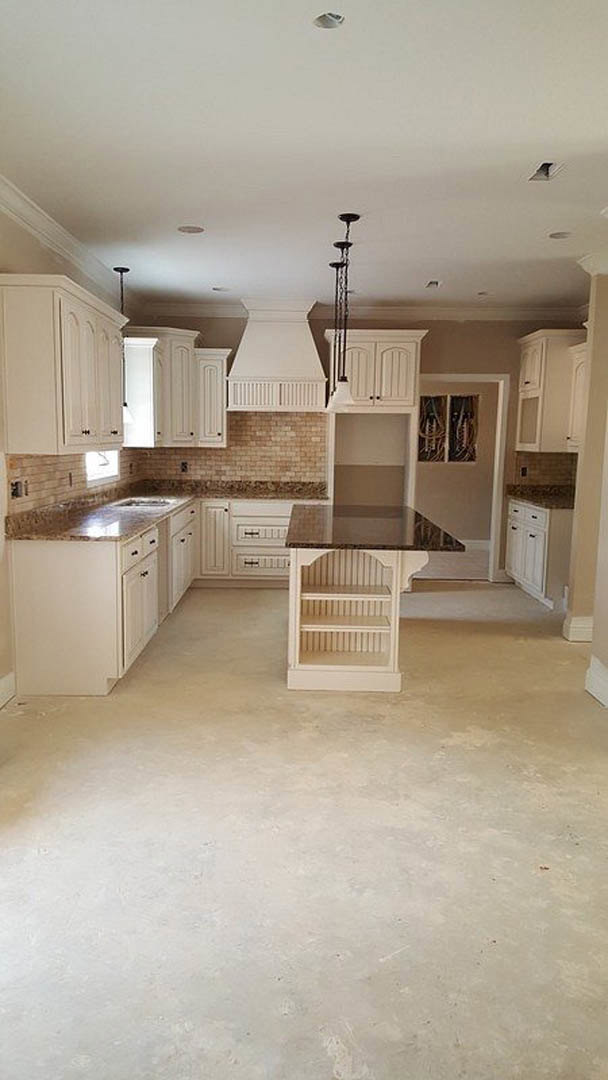 White kitchen featuring marble countertops, white cabinetry, central island with marble surface, stainless steel sink, and vent hood against a white wall