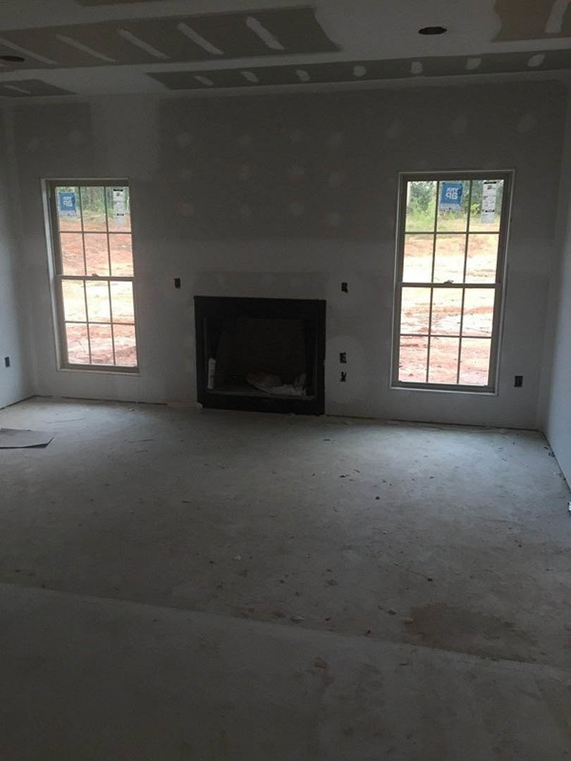 Living room with plaster walls, large windows, modern black fireplace, hardwood flooring, and open staircase.