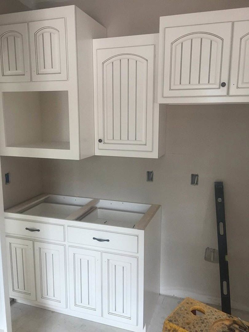 White kitchen cabinets with shaker-style doors and drawers, stainless steel appliances, light stone countertops, and a white paneled door in the background.