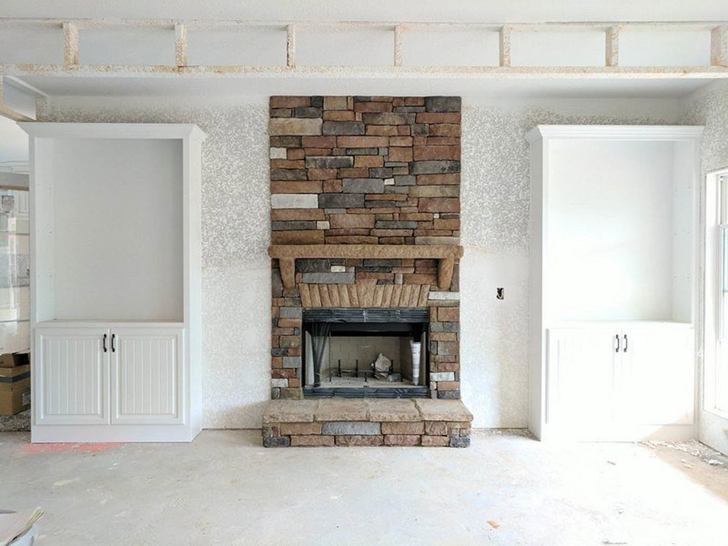 Stone fireplace with white cabinetry featuring black handles, white walls, and built-in shelving in a modern living room.