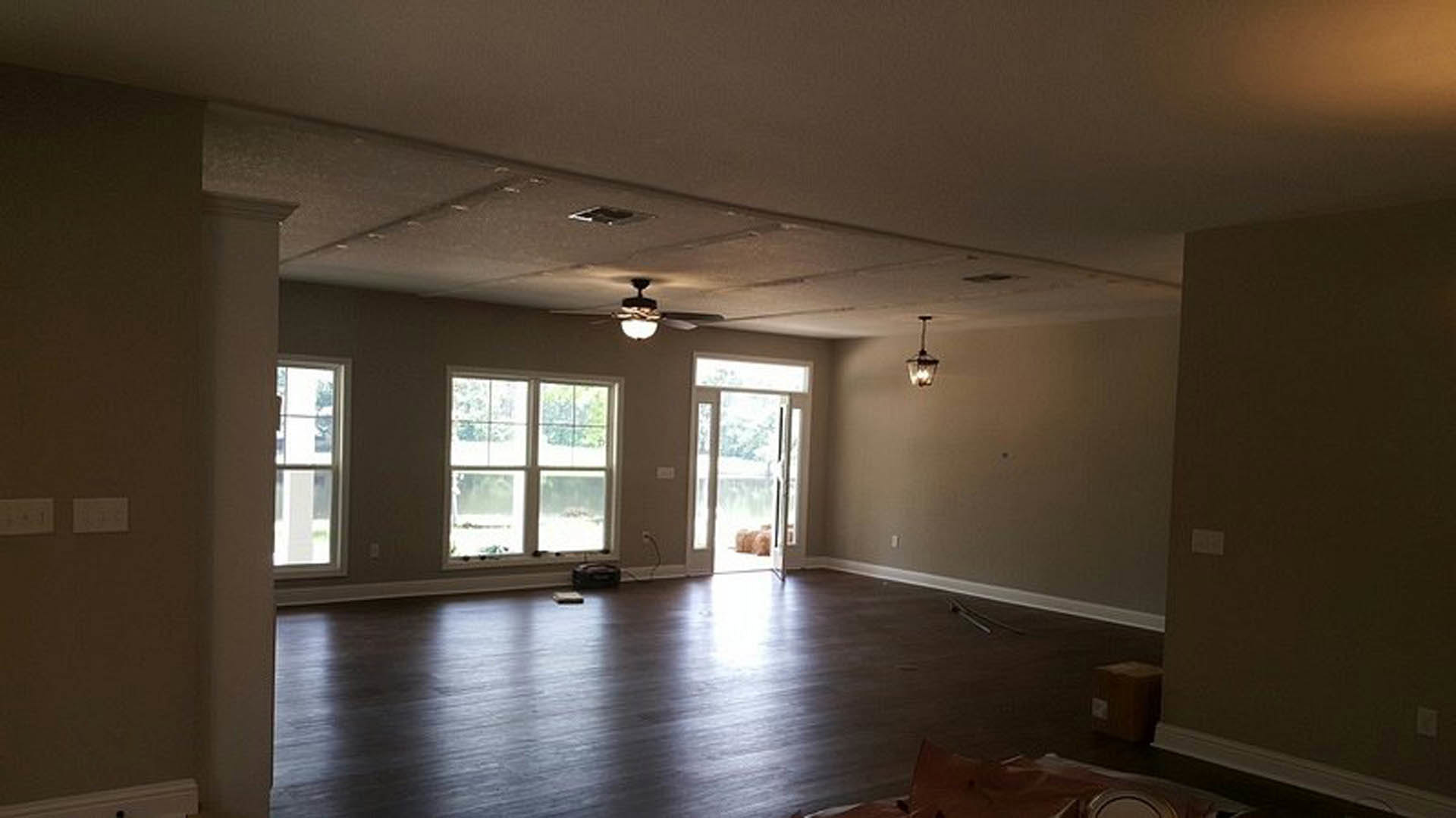 Living room with wood plank flooring, white walls, ceiling fan, and light switch near doorway