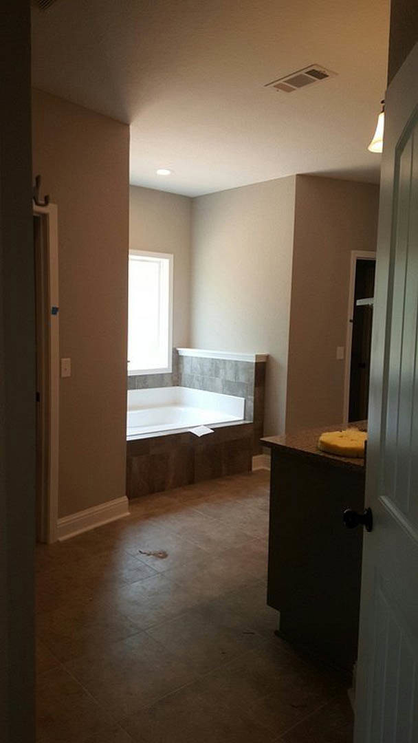 Modern bathroom featuring a white rectangular bathtub, sleek white sink with cabinetry, light plaster walls, tiled flooring, and recessed ceiling lighting.
