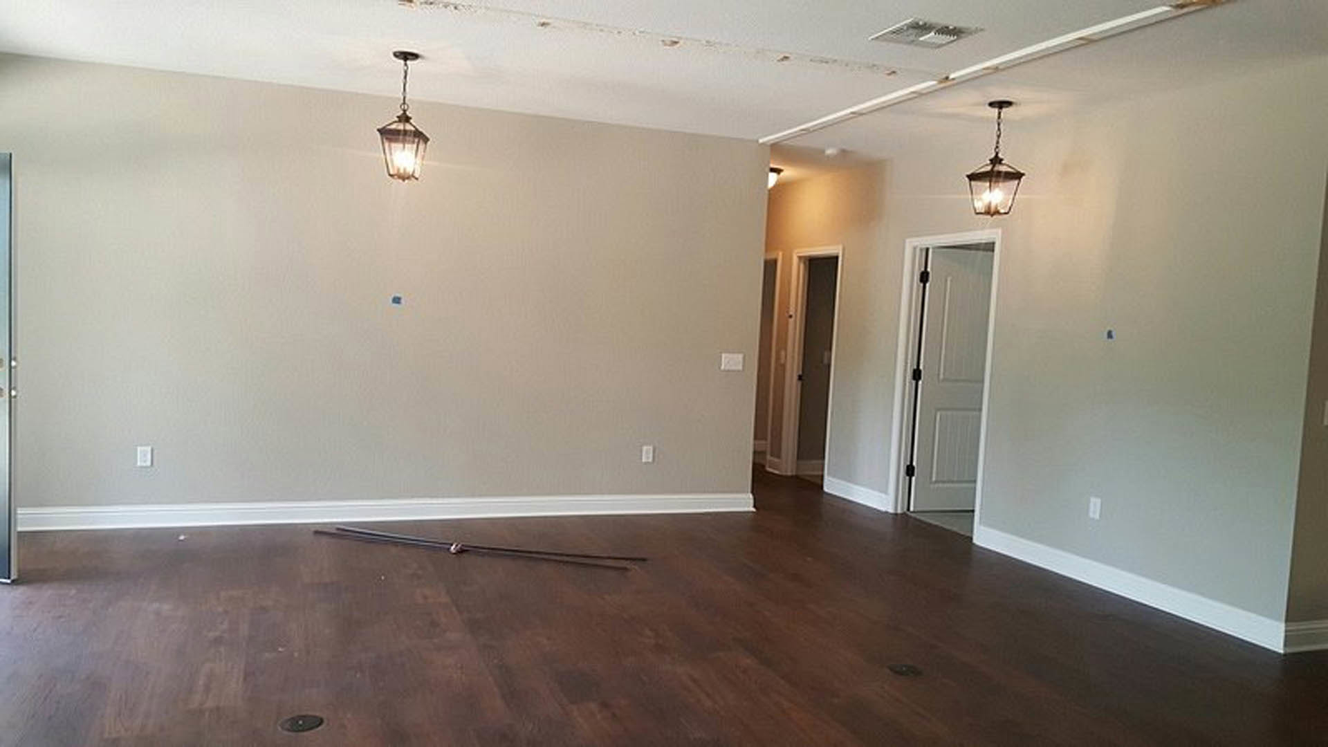 Wood plank flooring and matching wood ceiling, white plaster walls, white door with black handle, close-up of a modern lamp, natural light highlighting finishes