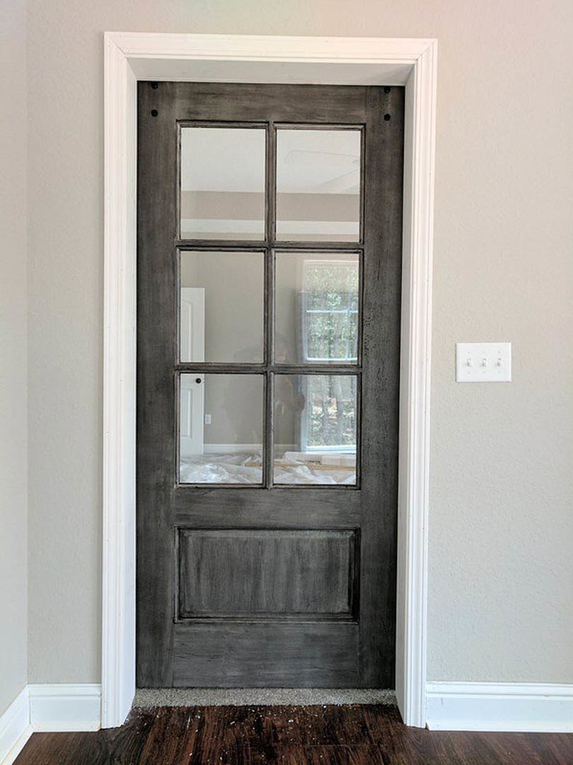 Wooden door with multiple glass panes, white trim, adjacent white wall with light switch, hardwood flooring