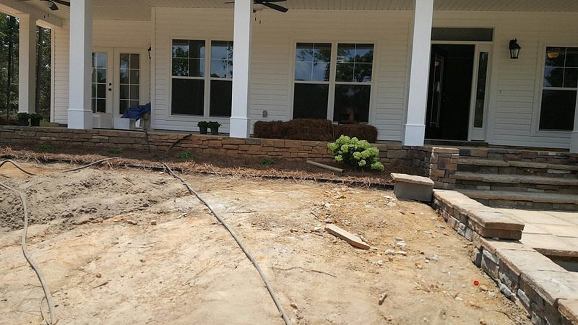 Two-story house with large windows and covered porch, surrounded by bare dirt yard with scattered sticks and construction materials.