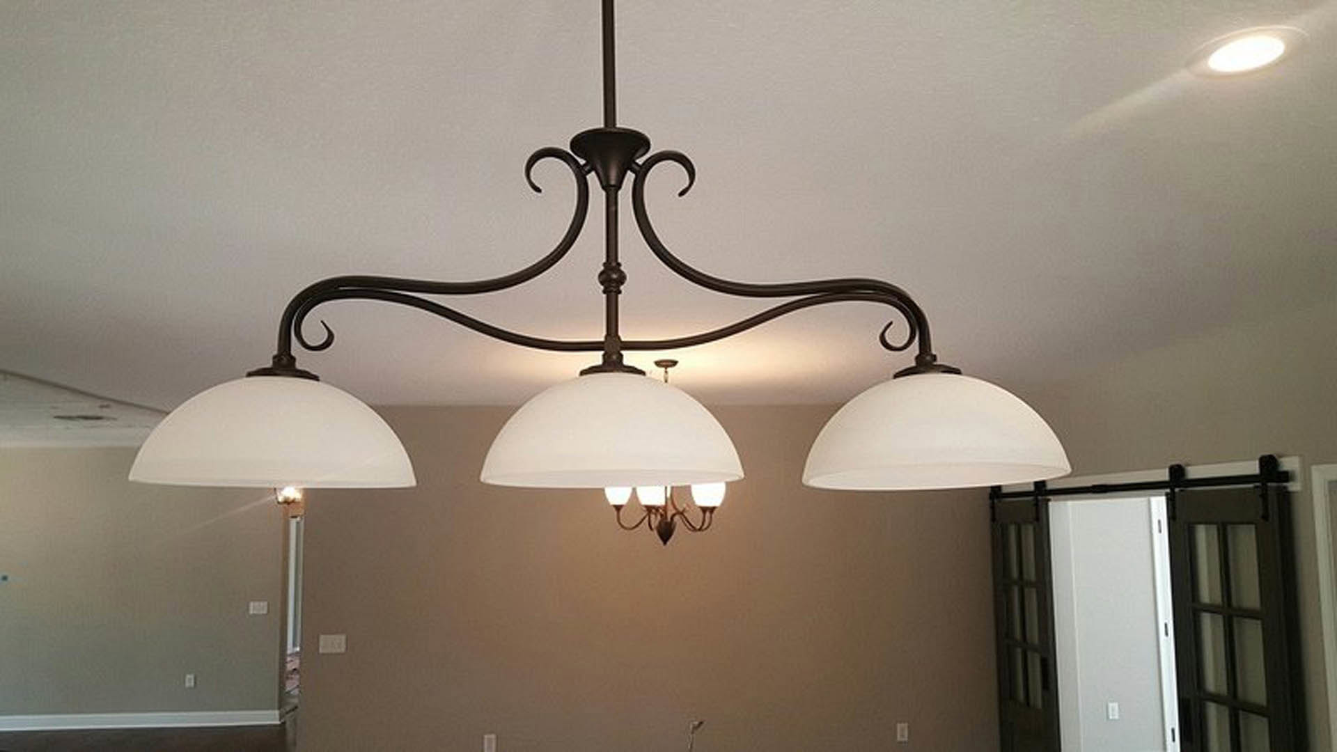 Brushed metal ceiling fixture with three frosted glass shades, mounted above neutral painted walls in a modern living space