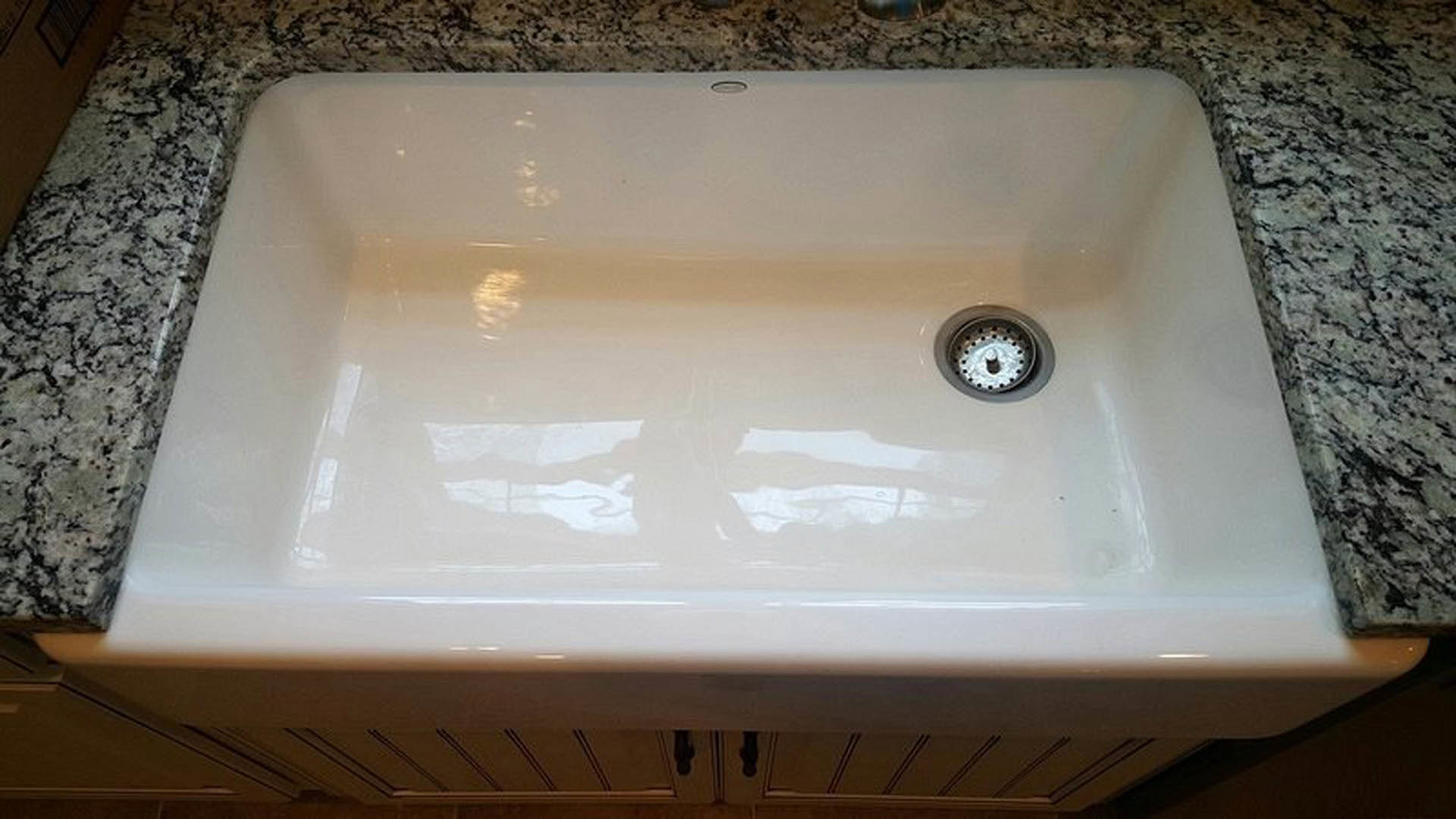 White porcelain bathroom sink with chrome drain set in a light countertop, partial view of faucet and tiled wall in background.