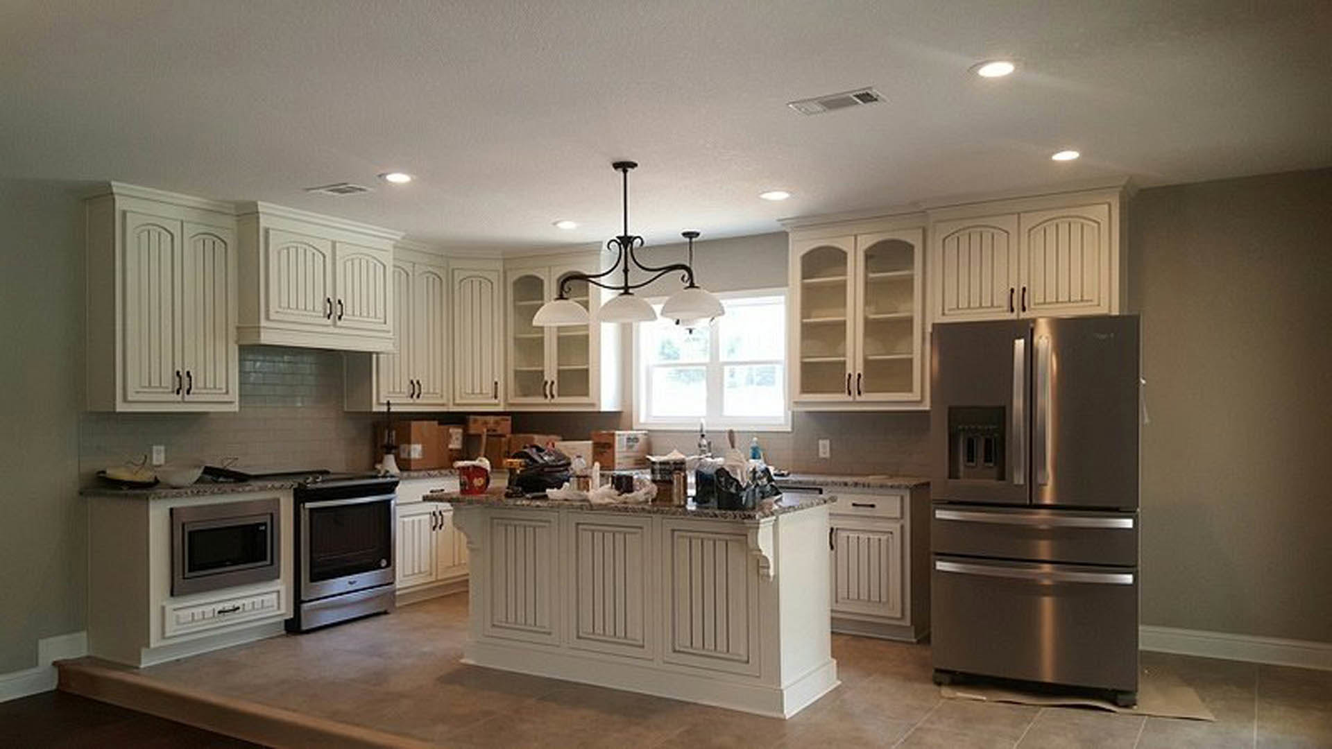 White kitchen cabinets with stainless steel refrigerator, black door microwave, and modern light fixture above a quartz countertop