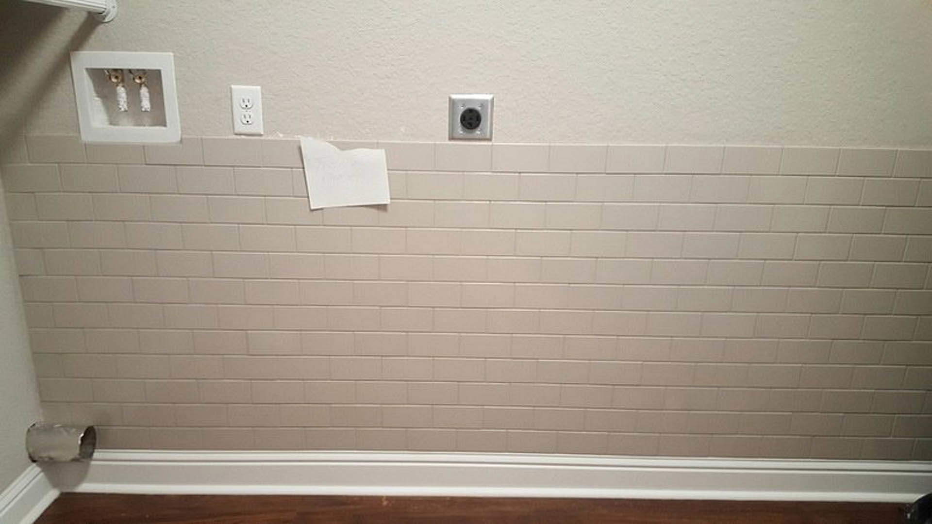 White tile bathroom wall adjacent to smooth white plaster wall with a single white piece of paper taped near the corner.