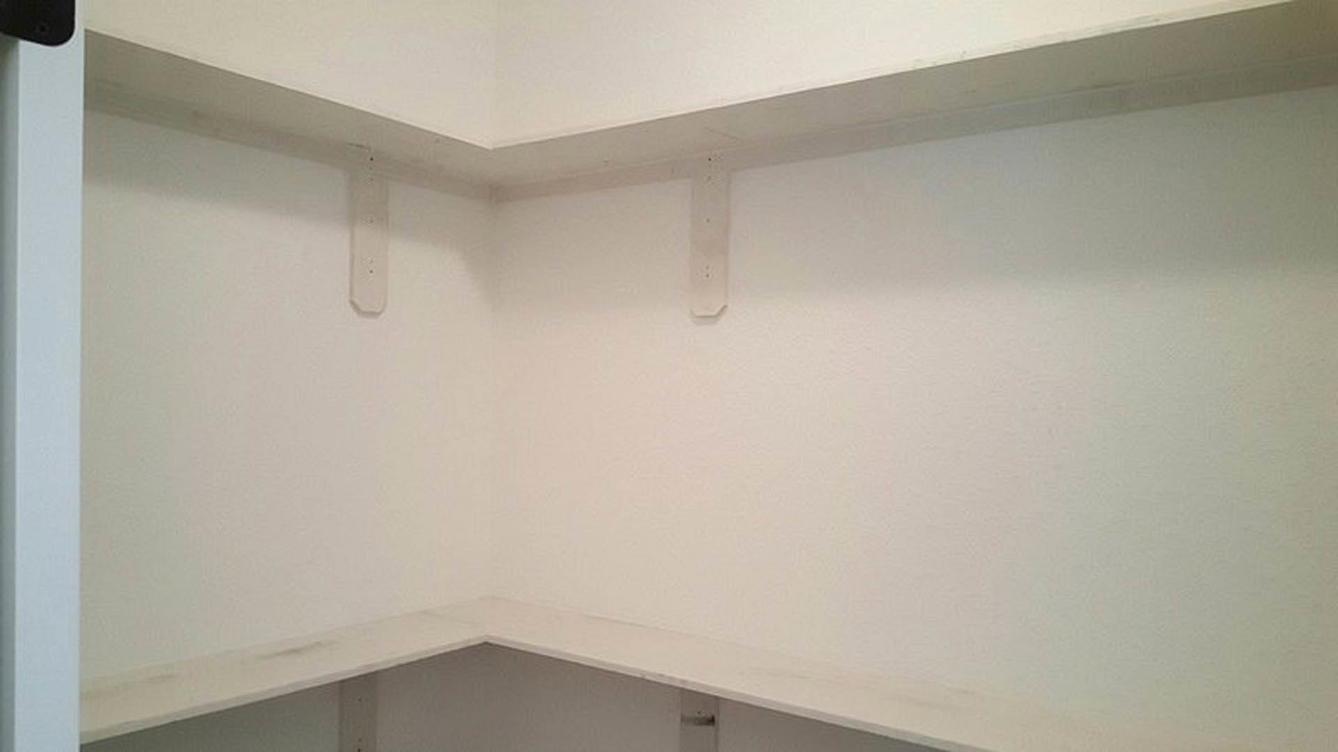 White built-in shelves against a smooth white plaster wall, adjacent to a white ceiling and room corner, with a small black spot visible on the wall.