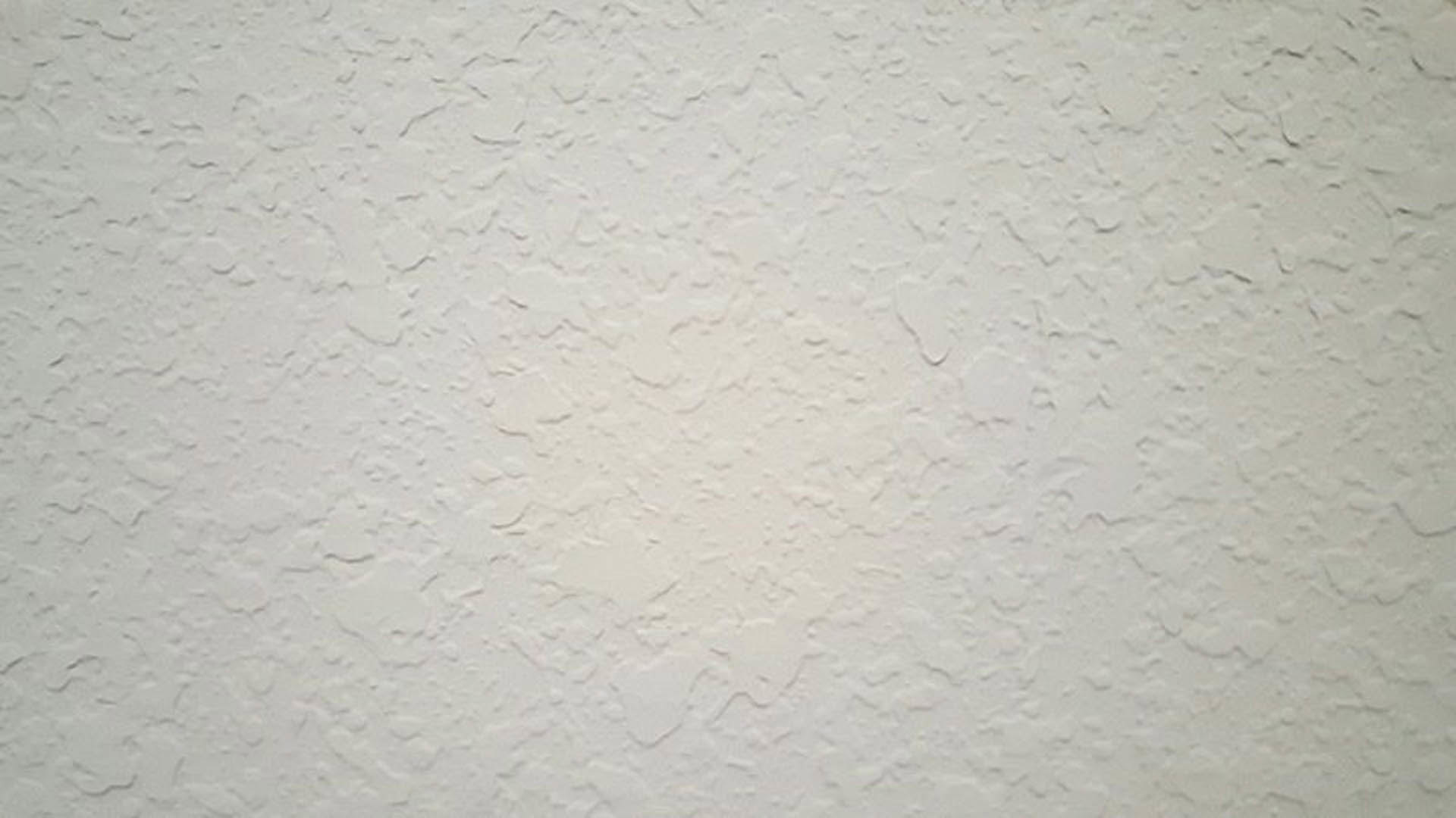 Close-up of a white wall with a rough texture and small grey spots