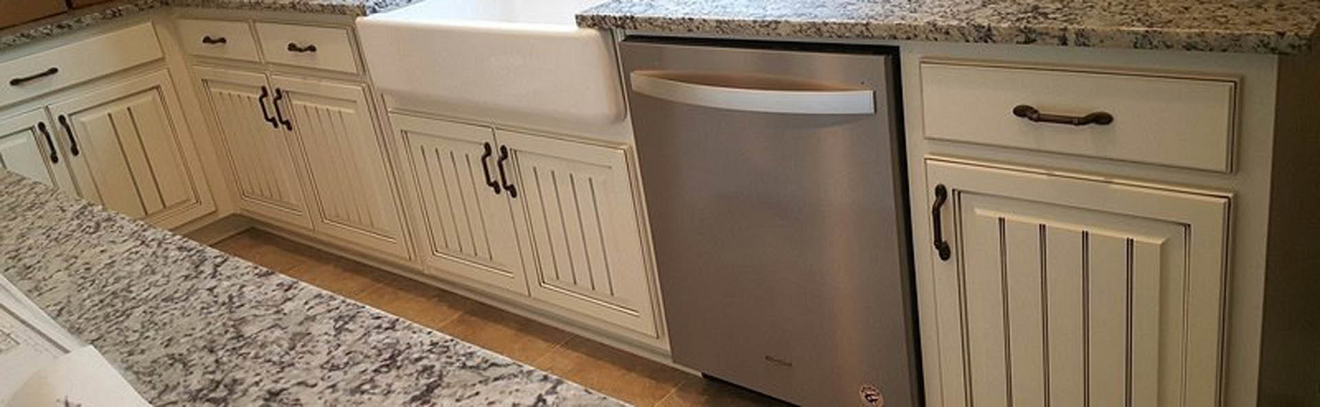 Stainless steel dishwasher with handle beside undermount sink, white countertop, light cabinetry, and tiled backsplash
