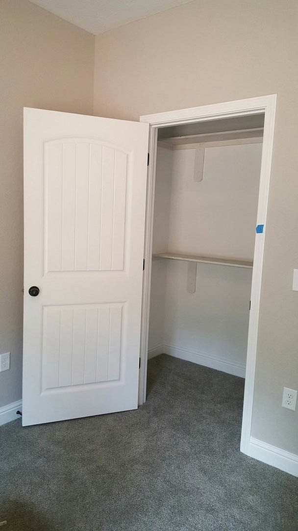 Open white closet door with black knob, grey carpeted floor, built-in shelf and white cabinetry inside closet