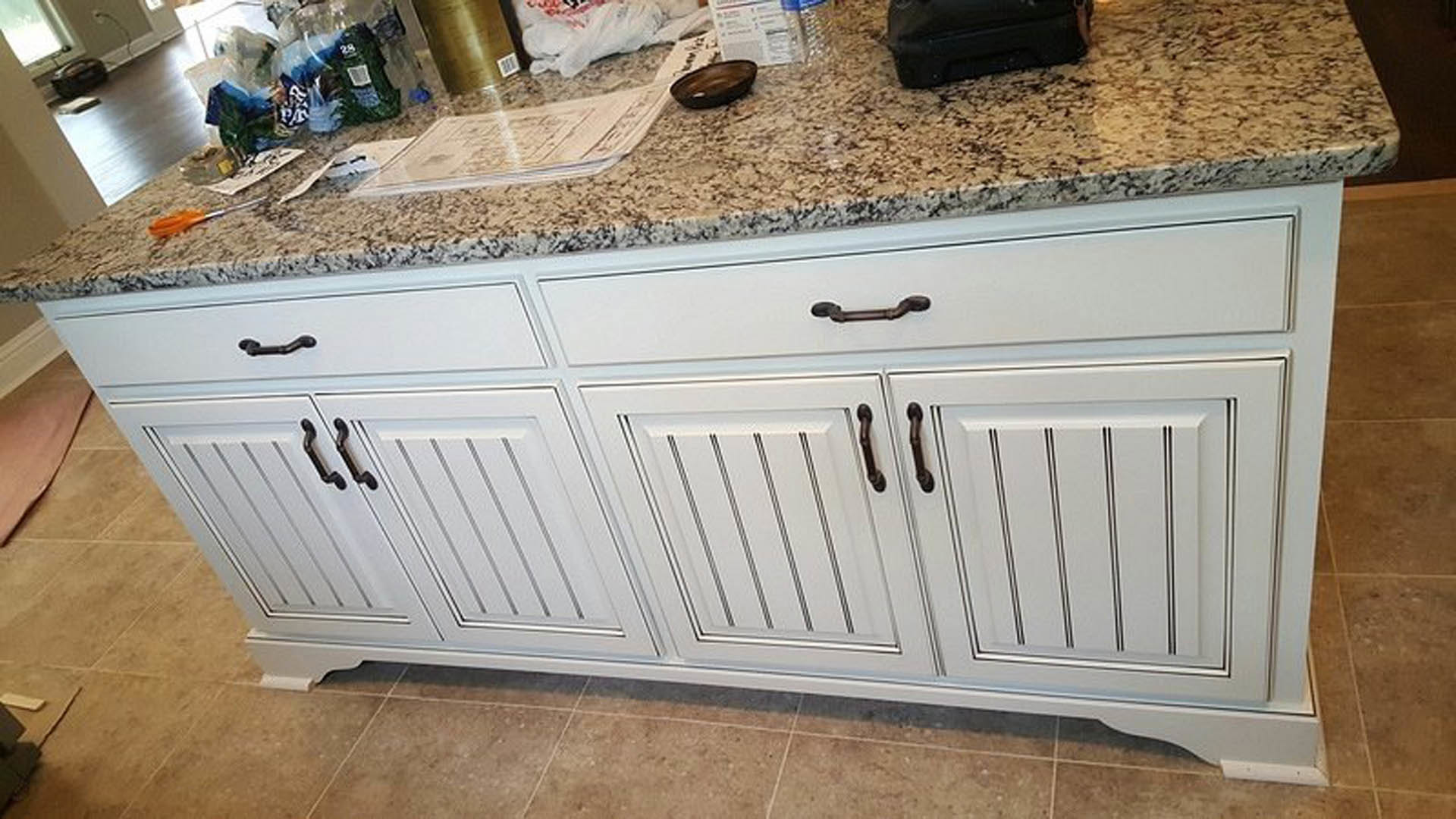 Marble kitchen island with white cabinetry, stainless steel sink, and chrome faucet on light wood flooring
