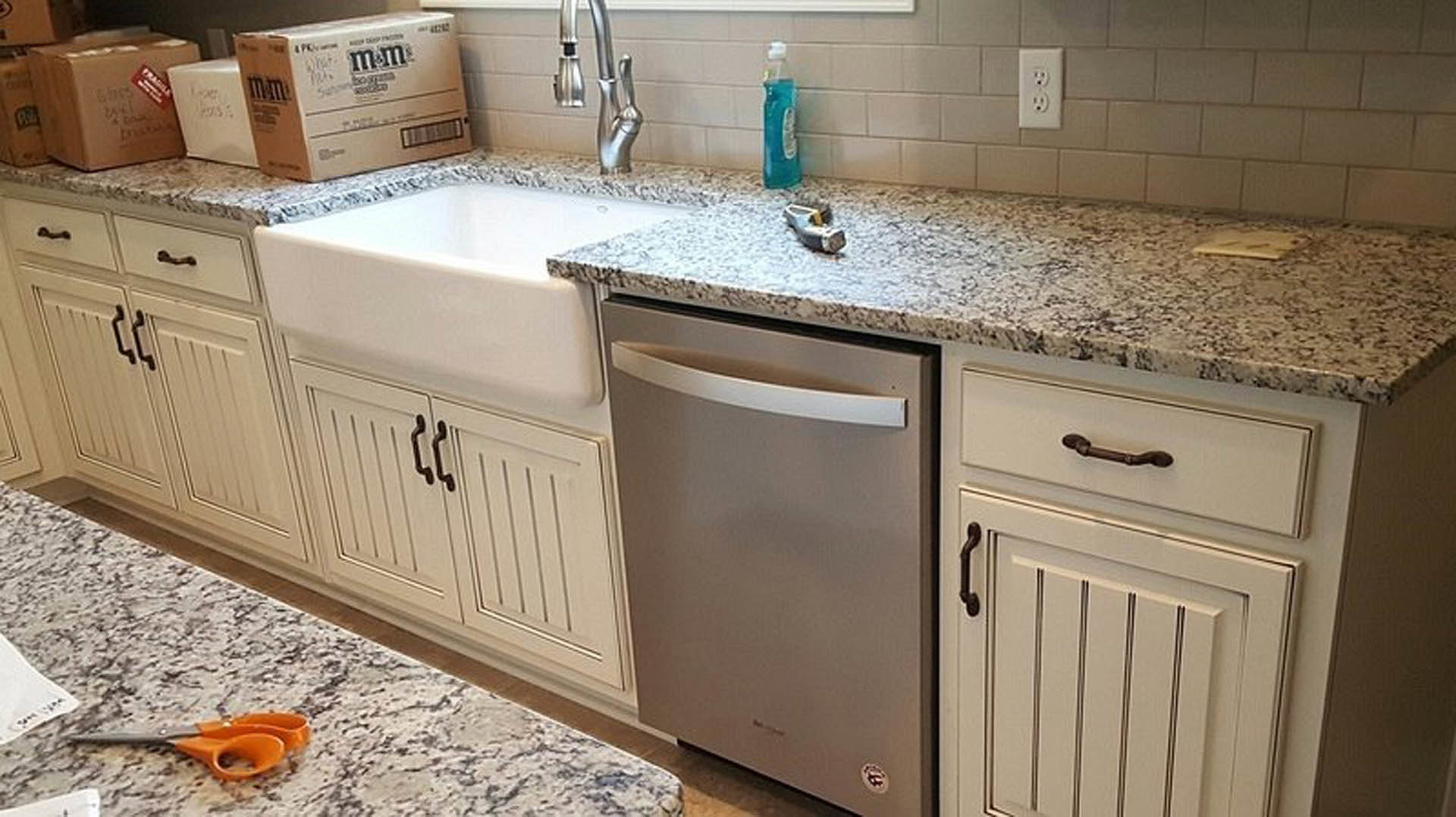 White kitchen sink with marble countertop edge, stainless steel dishwasher, tile backsplash, white cabinetry, and drawers