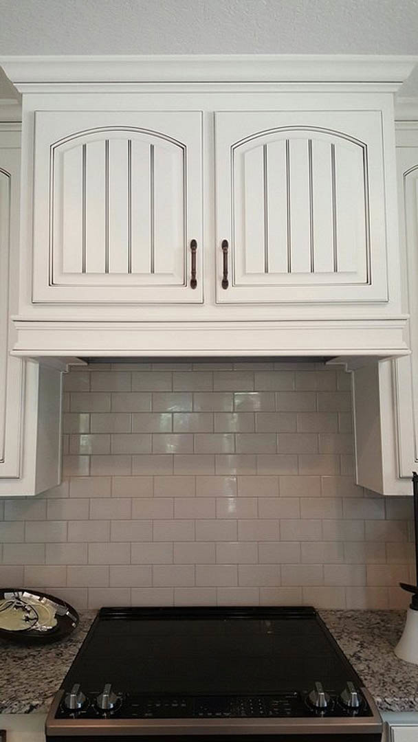 White kitchen with shaker cabinets, subway tile backsplash, gas cooktop, built-in microwave, white floating shelf, and contrasting black electronic device on countertop.