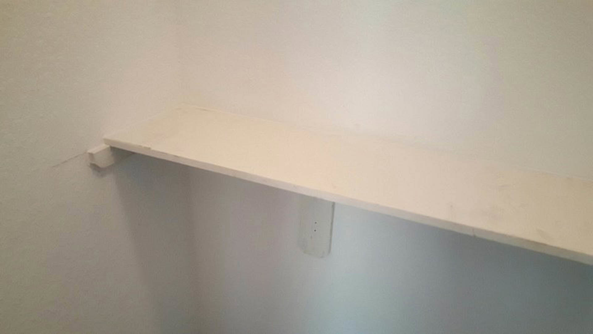 White plaster wall with built-in white shelf and exposed pipe in a residential room