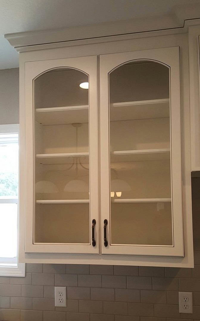 White cabinet with glass doors, white outlet with black holes, white door with window, close-up of glass door and door handle, light-colored walls and ceiling, shelving, and