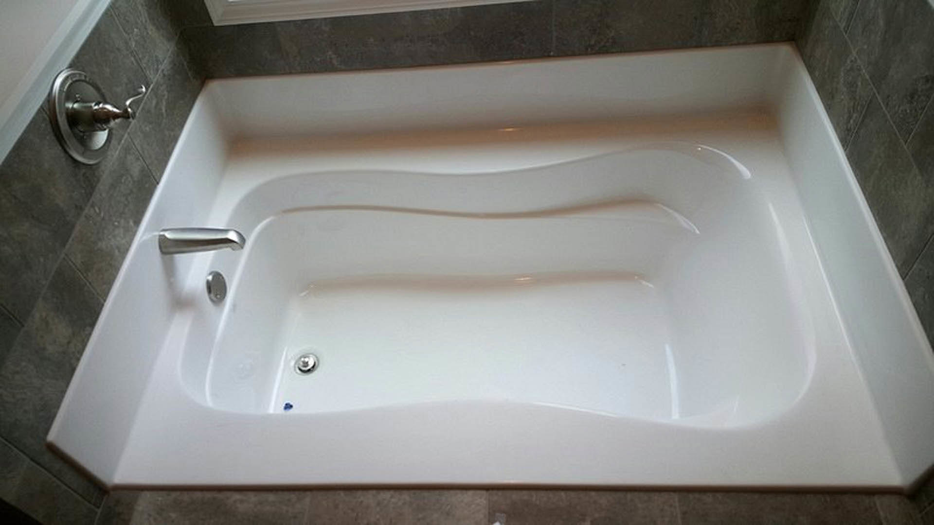 White curved bathtub with silver faucet, surrounded by light tile walls and bathroom accessories