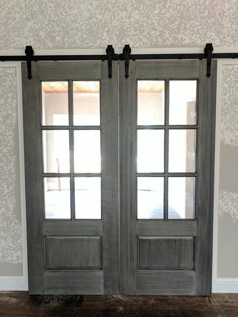 Black-framed double doors with glass panes, matte black door handles, adjacent light gray wall, and reflective window surfaces