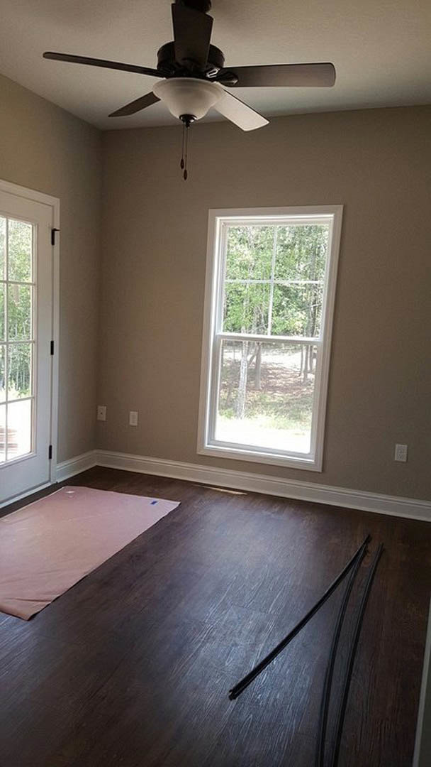 Wood floor with a pink sheet and piece of paper, white door with black handle, window showing trees outside, ceiling fan with light fixture