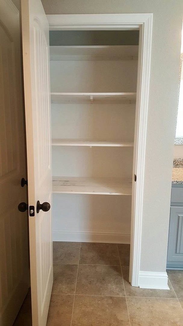White built-in closet with open shelves, silver door handle, and light tile flooring