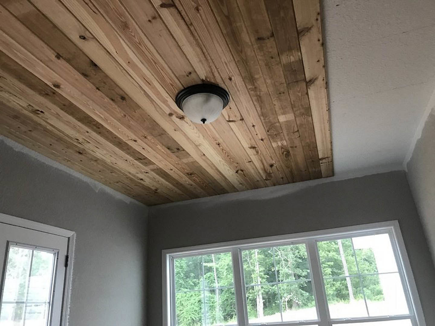 Wood paneled ceiling with recessed light fixture, large window framed by molding, view of trees outside
