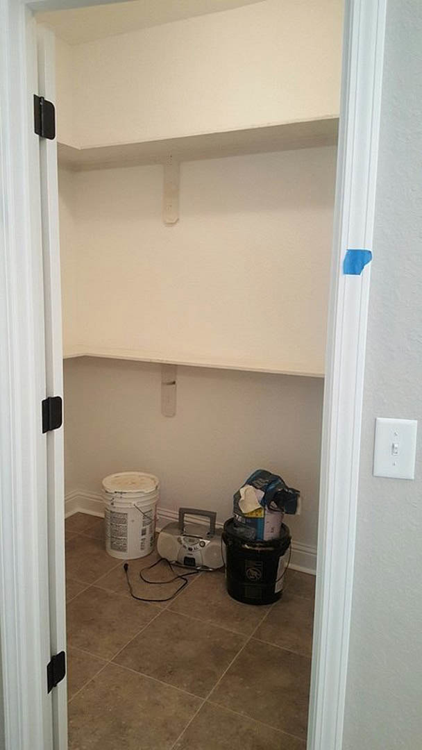 Closet with multiple white and black buckets, blue object inside one bucket, radio with handle on shelf, light switch on plaster wall, close-up of a hat, wood floor, cabinetry, and
