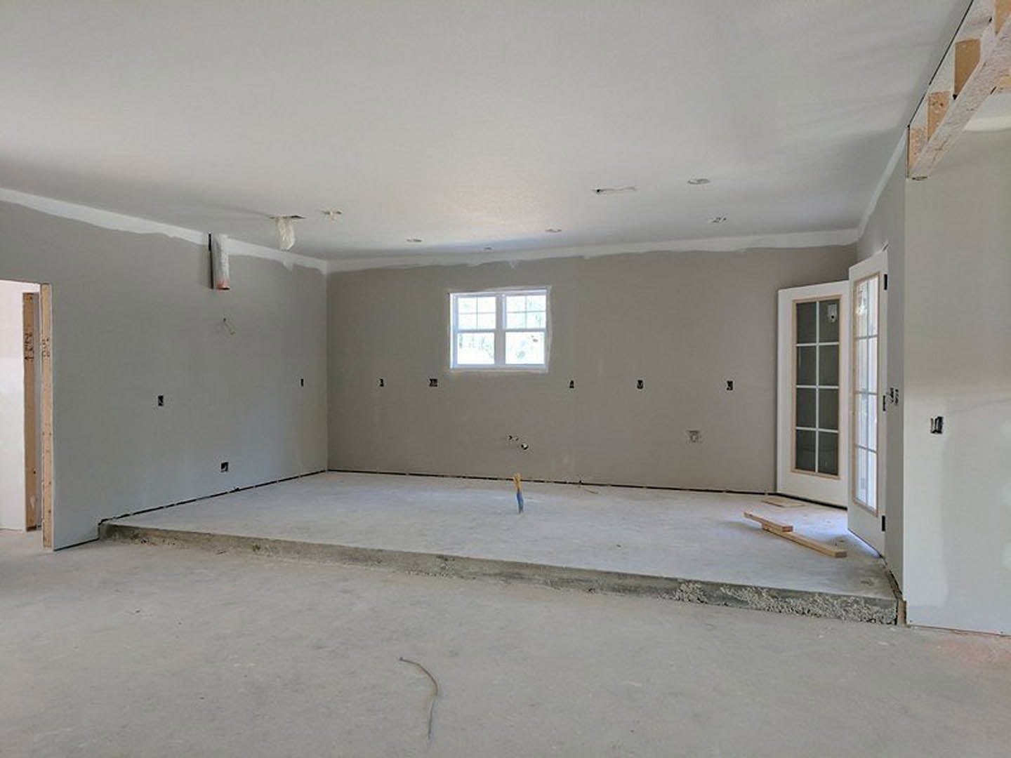 Concrete floor room with plaster walls, glass-paneled door, exposed ceiling, window, and visible electrical wiring on slab