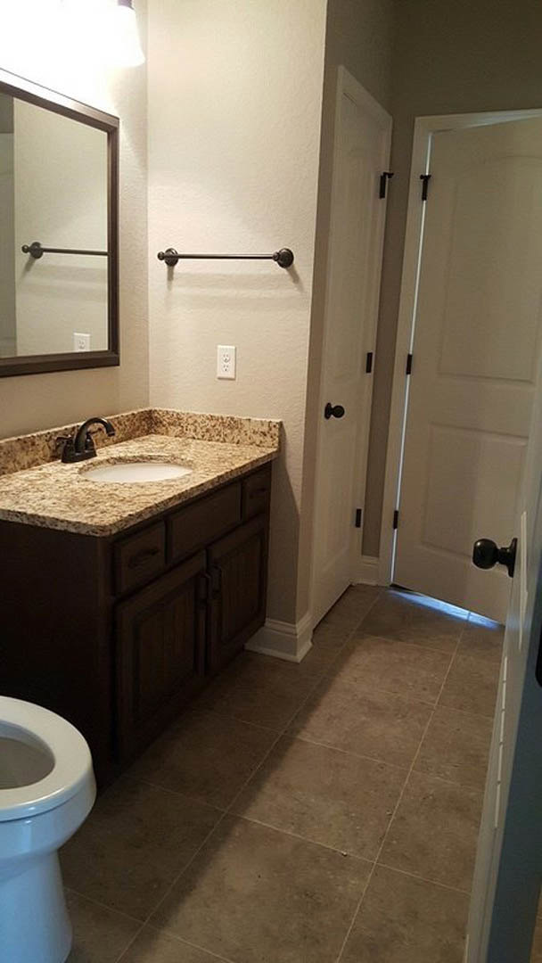 Modern bathroom with white tile walls, rectangular mirror above a sleek vanity sink, chrome faucet, and partial view of a toilet on tiled floor