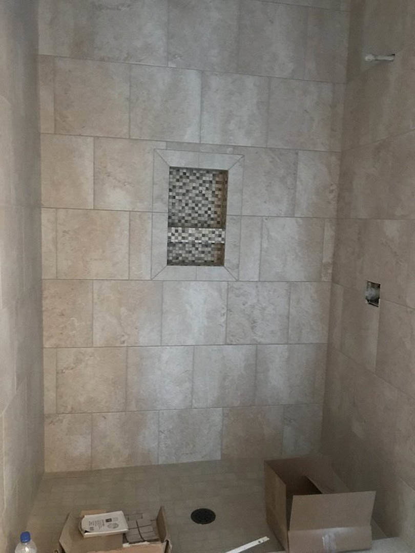 Shower with large-format gray tile wall, glass enclosure, chrome fixtures, and built-in niche for toiletries