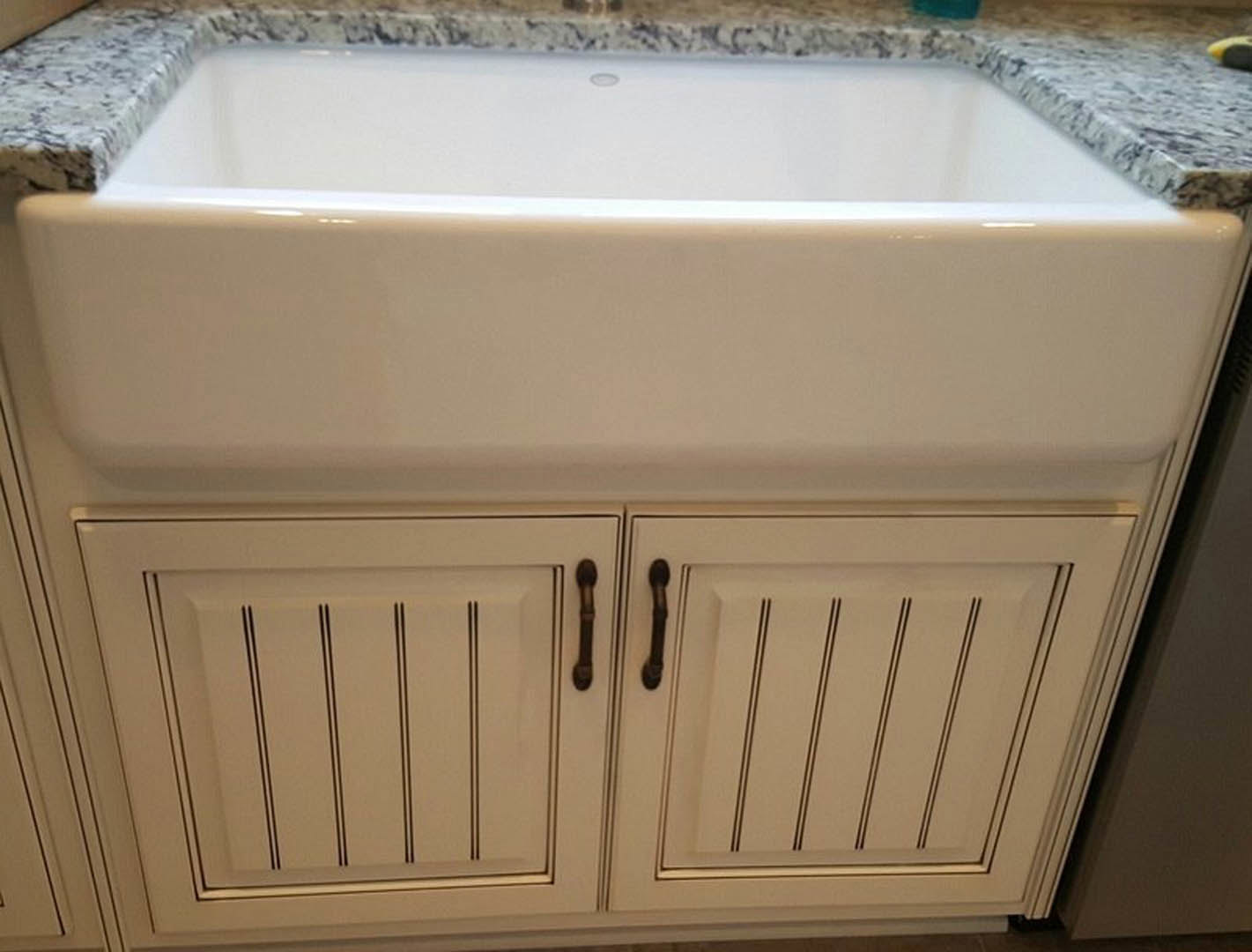 White undermount sink set in a polished marble countertop with subtle gray veining, adjacent to a white cabinet featuring black trim.