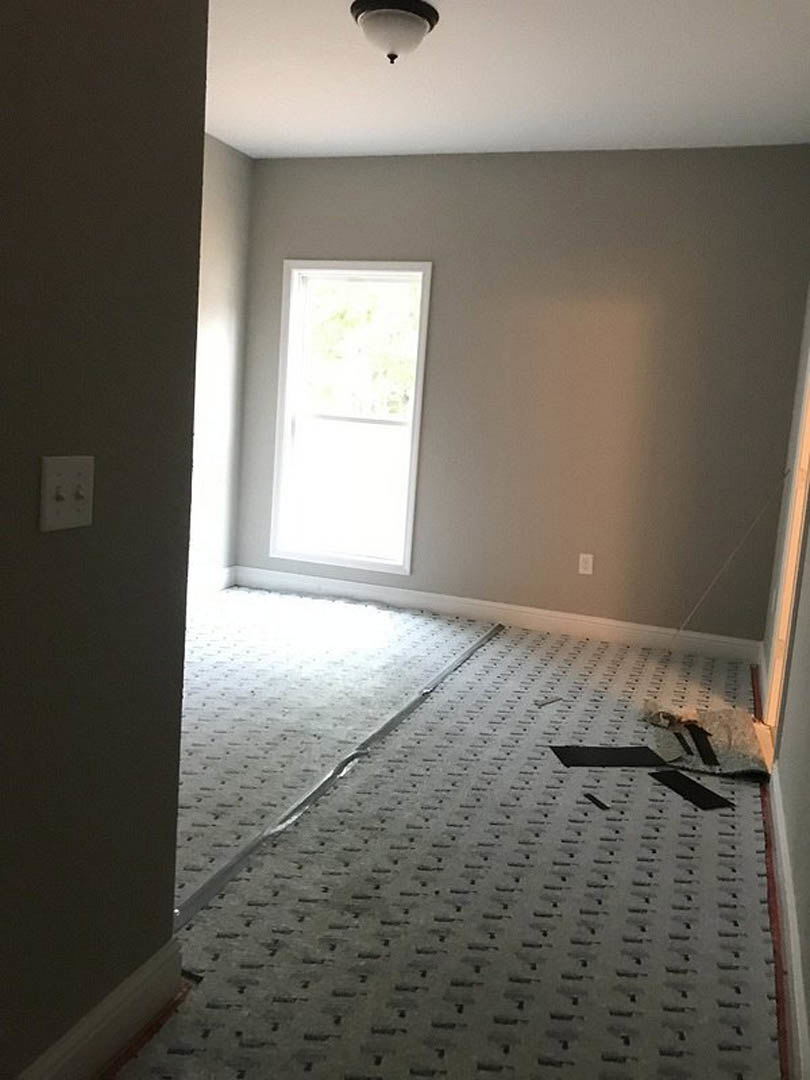 Carpeted room with white door and frame, window with white trim, light switch on wall, ceiling fan, and laminate flooring section with visible hole