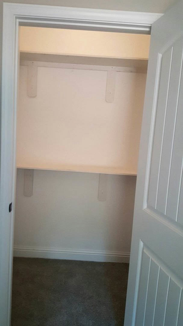 Walk-in closet with white shelving, carpeted floor, white door with silver handle, and smooth white walls