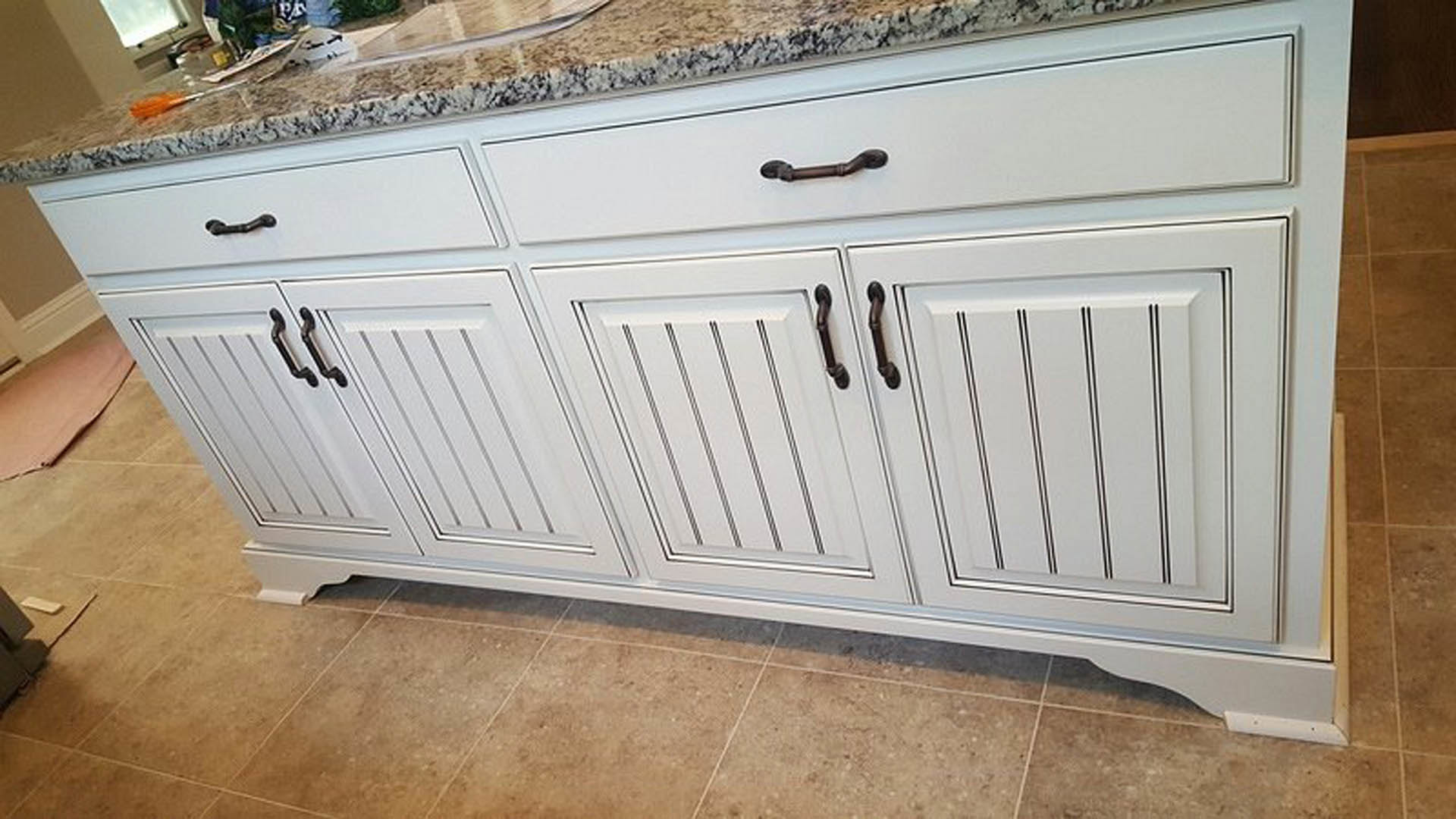 White kitchen cabinets with black handles, light tile flooring, wood countertop, and neutral walls