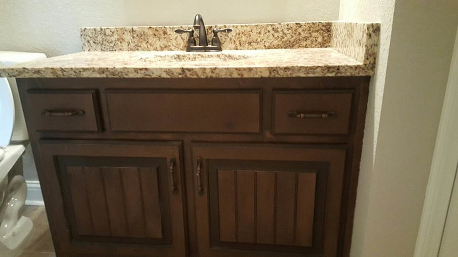 Marble countertop with undermount sink, chrome faucet, white cabinetry, and tiled backsplash in a kitchen or bathroom