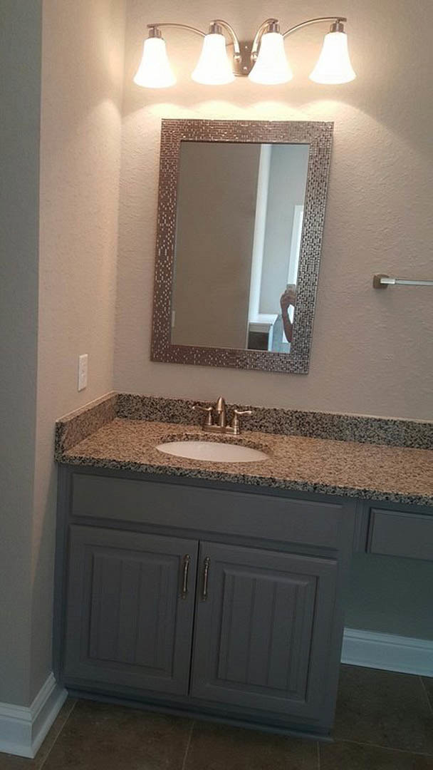 White bathroom with rectangular mirror above a quartz countertop, undermount sink, chrome faucet, and double light fixture mounted on light gray wall.